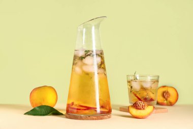 Bir sürahi taze şeftali ve limonata, yeşil arka planda bej masa üzerinde kekik.