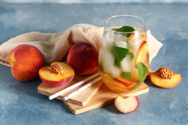 Bir bardak taze şeftalili limonata, nane ve mavi arka planda meyveler.