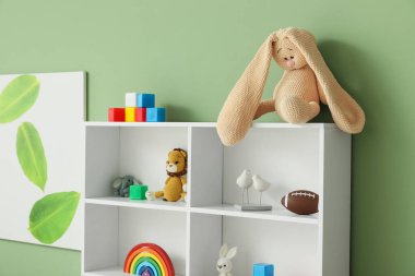 Yeşil duvarın yanında çocuk oyuncakları olan raflar.