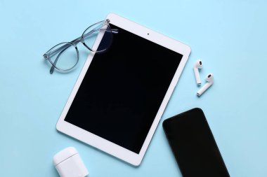 Modern tablet bilgisayar, cep telefonu, kulaklık ve gözlük mavi arka planda, yakın plan