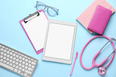 Tablet bilgisayar, klavye, steteskop ve mavi arkaplan üzerine not defterleri, yakın plan