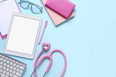 Tablet bilgisayar, klavye, steteskop ve mavi arkaplan üzerine not defterleri, yakın plan