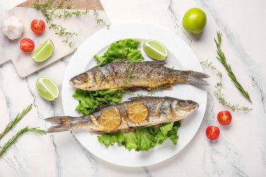 Lezzetli pişmiş deniz kabuğu balığı, marul, otlar, domatesler ve mermer zemin üzerinde limon dilimleri.