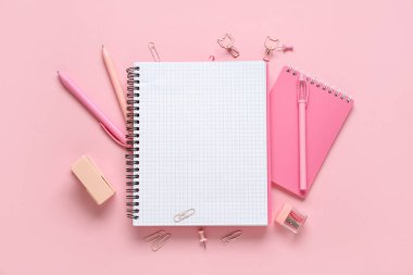 Pembe arka planda boş defter ve okul kırtasiyesine sahip kompozisyon