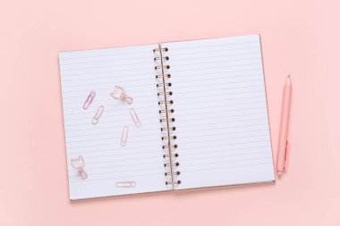 Boş bir defter, ataç ve pembe arka planda bir kalem.