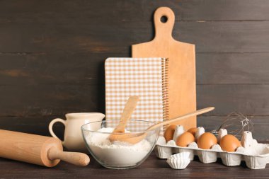 Farklı pişirme aletleri, malzemeler ve kahverengi ahşap arka plandaki defter.