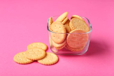 Pembe arka planda lezzetli krakerler olan cam kase, yakın plan.