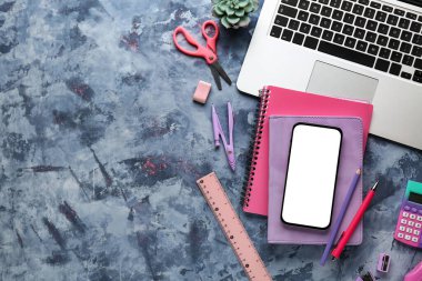 Mavi grunge arka planında okul kırtasiyesi, modern dizüstü bilgisayar ve cep telefonu ile kompozisyon