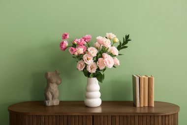 Çok güzel Eustoma çiçekleri olan vazo, heykel ve oturma odasındaki çekmeceler üzerine kitaplar.