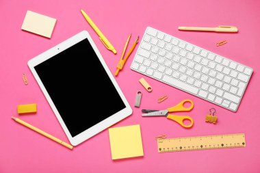Pembe zemin üzerinde tablet bilgisayar, klavye, kırtasiye ve modern flaş bellek bileşimi