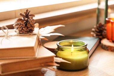 Kitaplar, kuru yapraklar ve yanan mum oturma odasındaki pencerenin yanında, yakın plan.