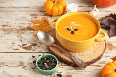 Tahta arka planda tohumlu, sarımsaklı ve kaşıklı lezzetli balkabağı kremalı çorba.