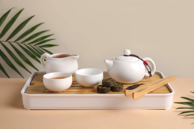 Çaydanlık, fincanlar ve tropikal yapraklarla bej masa, yakın plan çay seremonisi için ayarlandı.