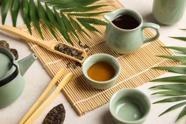 Bej rengi grunge arka planda sürahi, fincan ve tropikal yapraklarla çay seremonisi için hazırlandı. Yakın plan.