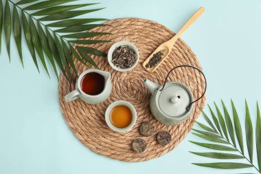 Çaydanlık, fincan ve tropikal yapraklı çay seremonisi için mavi arka planda, yakın plan