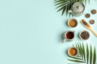 Çaydanlık, fincanlar ve tropikal yapraklarla mavi arka planda çay seremonisi yapılacak.