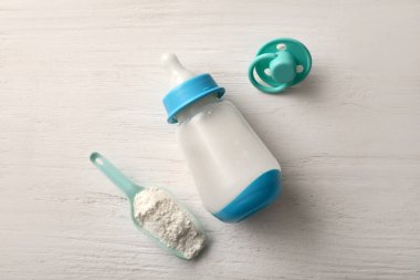 Beyaz ahşap zemin üzerinde emzik ve şişe ile bebek sütü formülü kepçesi