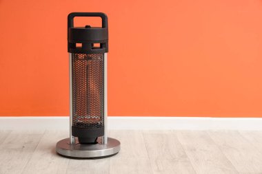 Turuncu duvarın yanındaki odada siyah elektrikli vantilatör ısıtıcısı var.