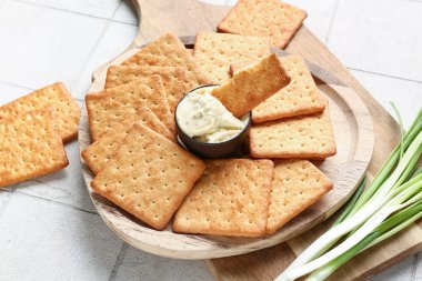 Tahta tahtalar, lezzetli krakerler, bir kase sos ve beyaz fayanslı yeşil soğan.