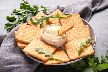 Lezzetli krakerler, bir kase sos, roka ve maydanoz ve siyah grunge arka planda.