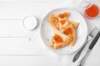 Beyaz ahşap zemin üzerinde kırmızı havyarlı, ekşi kremalı ve çatal bıçaklı leziz krepler.