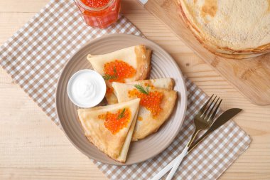 Kırmızı havyarlı leziz krepler, ekşi krema ve bej ahşap arka planda çatal bıçak takımı.