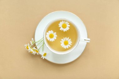 Bej arkaplanda bir fincan sıcak papatya çayı.