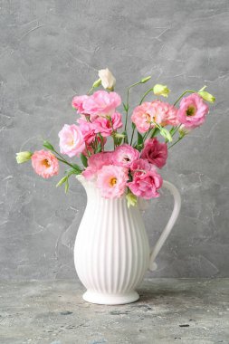 Gri arkaplanda pembe Eustoma çiçekleri olan bir sürahi.