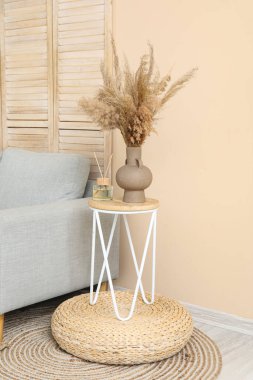 Şık gri kanepe, katlanır ekran, masa ve pampalar bej duvarın yanında.