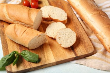Açık mavi arkaplanda taze baget, fesleğen ve kiraz domatesli ahşap tahta, yakın plan.