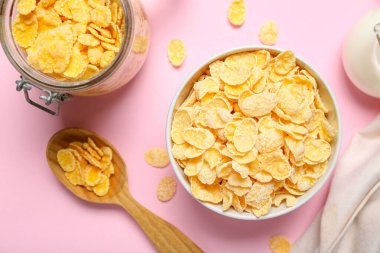 Pembe arka planda lezzetli mısır gevrekleri olan kase ve kavanoz, yakın plan.