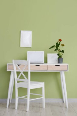 Ofisteki yeşil duvarın yanındaki masada güzel bir Anthurium çiçeği ve boş bir laptop.