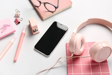Kulaklık, cep telefonu ve gri arka planda gözlüklü farklı kırtasiye malzemeleri.