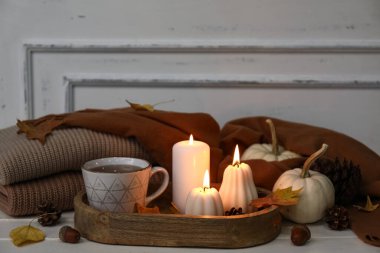 Yanan mumlar, bir fincan çay, elbiseler ve sonbahar dekoru olan kompozisyon