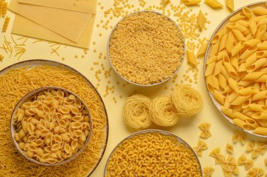 Bej arka planda farklı türde pişmemiş makarna içeren kaseler.