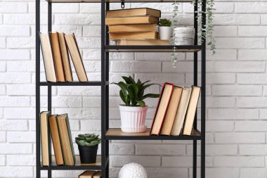Kitapları ve beyaz tuğla duvarın yanında dekorasyonu olan modern raf ünitesi, yakın plan.