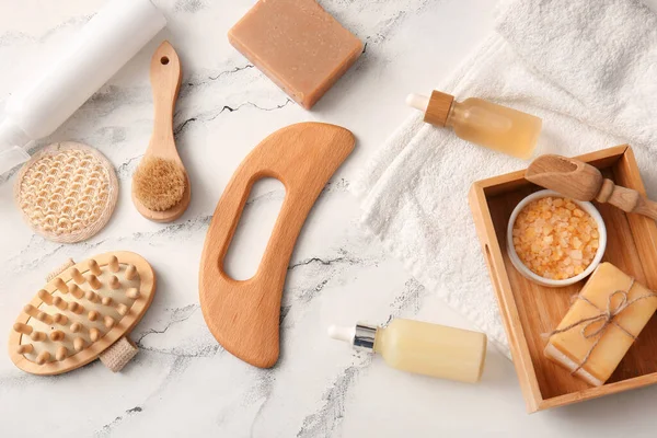 Ahşap guasha vücut masajı aracı, serum şişeleri ve mermer zemin üzerinde sabun çubukları ile kompozisyon