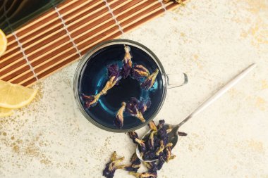 Bir fincan mavi organik çay ve arkaplanda kelebek çiçekli çay kaşığı, yakın plan.