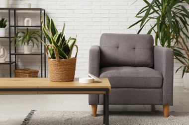 Oturma odasının iç tarafındaki beyaz tuğla duvarın yanında rahat bir koltuk, masa ve bitkiler.