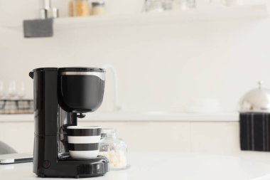 Mutfaktaki masada şeker ve fincanlı modern kahve makinesi.