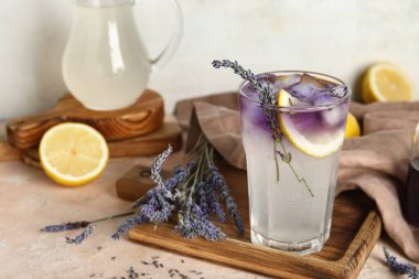 Tahta tahta tahta bir bardak soğuk lavanta limonata ve renkli masa üzerinde çiçekler.