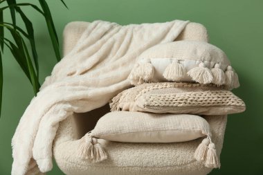 Yastıklı beyaz koltuk ve yeşil duvarın yanında saksı.