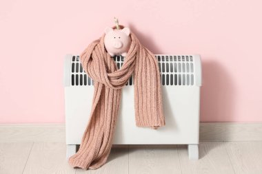 Domuz kumbarası ve pembe arka planda konteyner ısıtıcısı eşarbı. Isıtma kaydetme kavramı