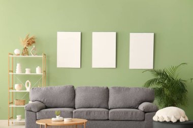 Rahat bir kanepe, sehpa ve yeşil duvarda boş posterler.