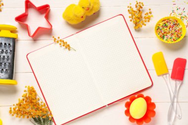 Boş tarif kitabıyla kompozisyon, pişirme araçları ve beyaz ahşap arka planda Paskalya dekoru