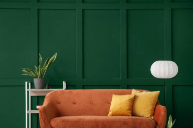 Oturma odasındaki yeşil duvarın yanında yastıkları olan rahat kahverengi kanepe.