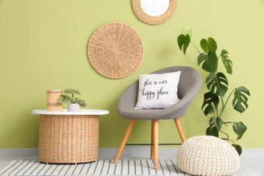 Oturma odasındaki yeşil duvarın yanında yumuşak puf ve masa olan rahat gri koltuk.