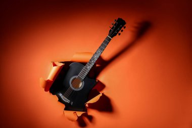 Siyah gitar turuncu kağıttaki delikten görülebilir.