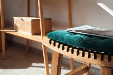 Oturma odasında zümrüt yastıklı ahşap tabure ve dergi, yakın plan.