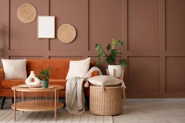 Oturma odasının içinde kanepe, hasır sepet, sehpa ve kahverengi duvarın yanında bitkiler var.